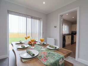 A dining area with a table set for breakfast, a view of the outdoors, and a kitchen in the background. - Sea View House (Redcar)