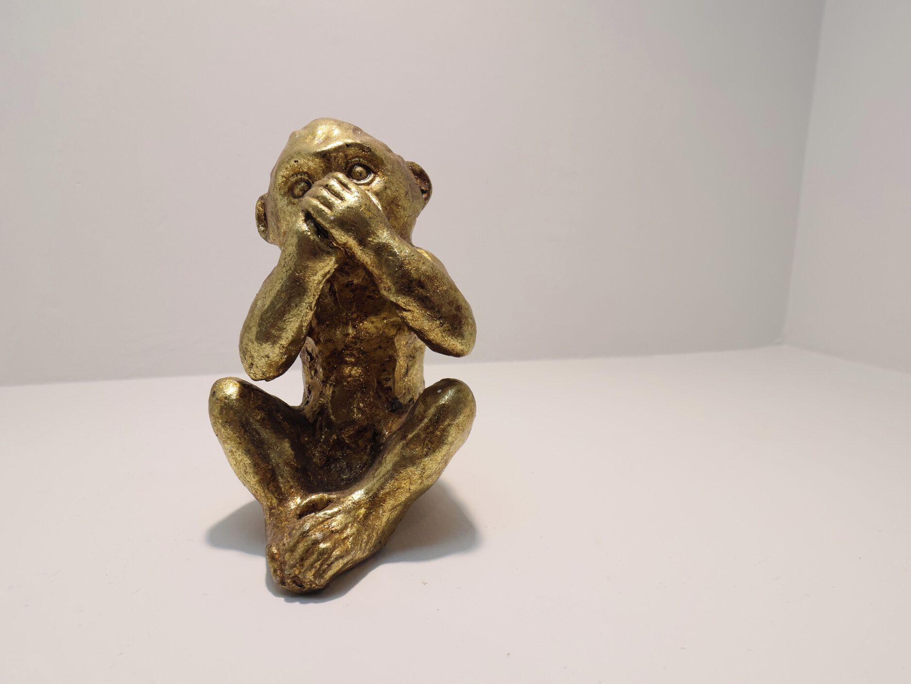 Une petite sculpture de couleur dorée représentant une figure assise, les mains couvrant le visage, posée sur une surface unie.