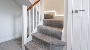 Eine Treppe mit hölzernem Geländer und Teppichstufen führt zu einer Tür mit silberner Klinke.