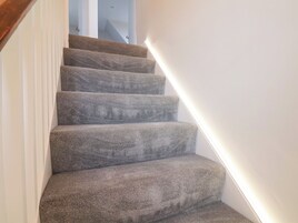 Una escalera alfombrada con barandilla de madera y una tira de luz a lo largo de la pared.