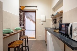 Cocina compacta con microondas, un lavamanos y un pequeño comedor con taburetes.