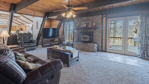 A spacious living room with a stone fireplace, leather furniture, and a large TV. - White River Escape with BBQ & Private Backyard (Norfork)