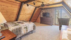 A cozy attic bedroom with a wooden ceiling, a bed with a quilt, a dresser, and a television. - White River Escape with BBQ & Private Backyard (Norfork)