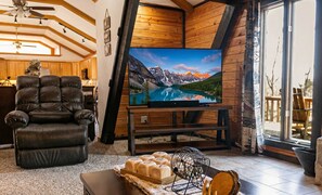Ett mysigt vardagsrum med en lädersoffa, ett soffbord i trä och en platt-TV som visar ett bergslandskap.
