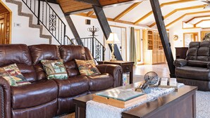 A spacious living room with a brown leather sofa, a wooden coffee table, and a staircase with a black railing. - White River Escape with BBQ & Private Backyard (Norfork)
