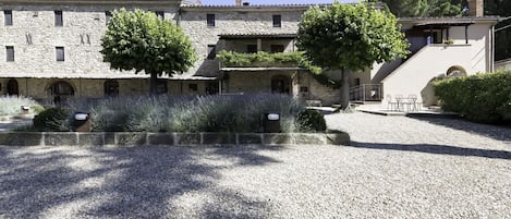 Edificio de piedra con patio, árboles y un camino de grava.