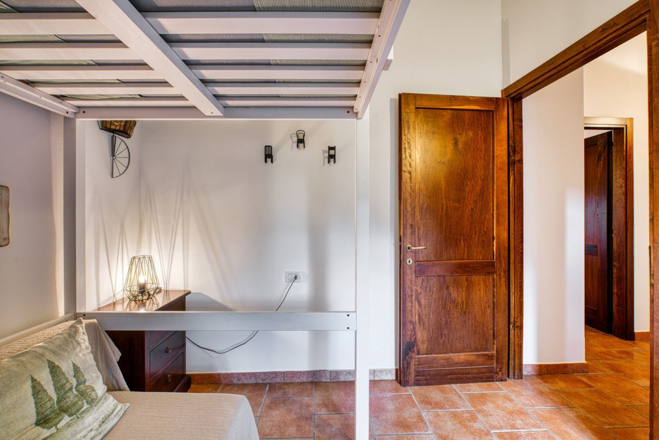 Une pièce avec un lit, un bureau, une porte en bois et un sol carrelé.