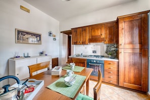A kitchen with wooden cabinets, a stove, and a dining table with chairs. - GuestHost - Cozy 50m2 apartment equipped with all comforts, ideal for two people, located on the second floor of a renovated farmhouse (stairs to access it).The accommodation is located inside a former oil mill and offers its guests many shared services: (Passignano sul Trasimeno)