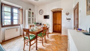 Zona pranzo con tavolo e sedie in legno, orologio, televisore e porta in legno.
