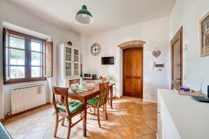 A dining area with a wooden table and chairs, a clock, a television, and a wooden door. - GuestHost - Cozy 50m2 apartment equipped with all comforts, ideal for two people, located on the second floor of a renovated farmhouse (stairs to access it).The accommodation is located inside a former oil mill and offers its guests many shared services: (Passignano sul Trasimeno)