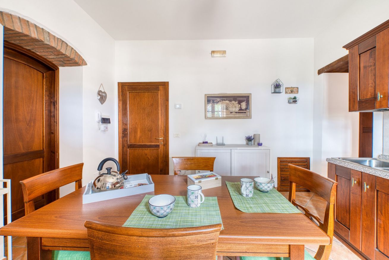 Un coin repas avec une table en bois, des chaises et une bouilloire. Il y a deux portes, un meuble et un tableau encadré au mur.