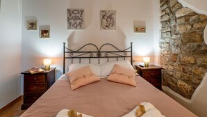Una camera da letto con parete in pietra, struttura del letto in metallo, due comodini con lampade e opere d'arte alle pareti.