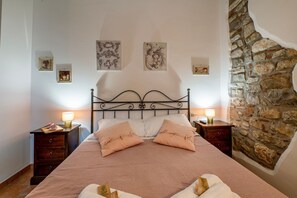 A bedroom with a stone wall, a metal bed frame, two bedside tables with lamps, and artwork on the walls. - GuestHost - Cozy 50m2 apartment equipped with all comforts, ideal for two people, located on the second floor of a renovated farmhouse (stairs to access it).The accommodation is located inside a former oil mill and offers its guests many shared services: (Passignano sul Trasimeno)