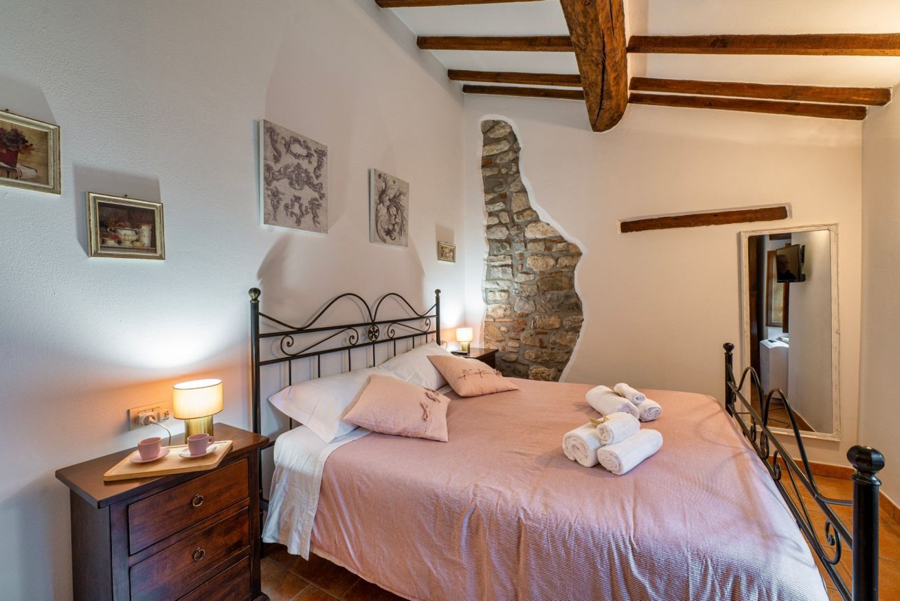 Ein Schlafzimmer mit Stehwänden, einem Bett mit rosa Bettwäsche, einem Nachttisch mit Lampe und einer Holzbalkendecke.