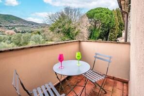 Een balkon met een ronde tafel en twee stoelen, twee wijnglazen en uitzicht op een glooiend landschap.