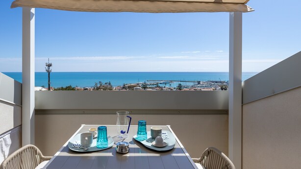 Een balkon met een tafel voor twee, met uitzicht op de kust, de zee en een pier in de verte.