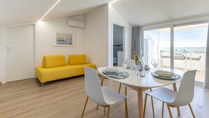 Een moderne kamer met een eettafel, witte stoelen, een gele bank en uitzicht op zee.