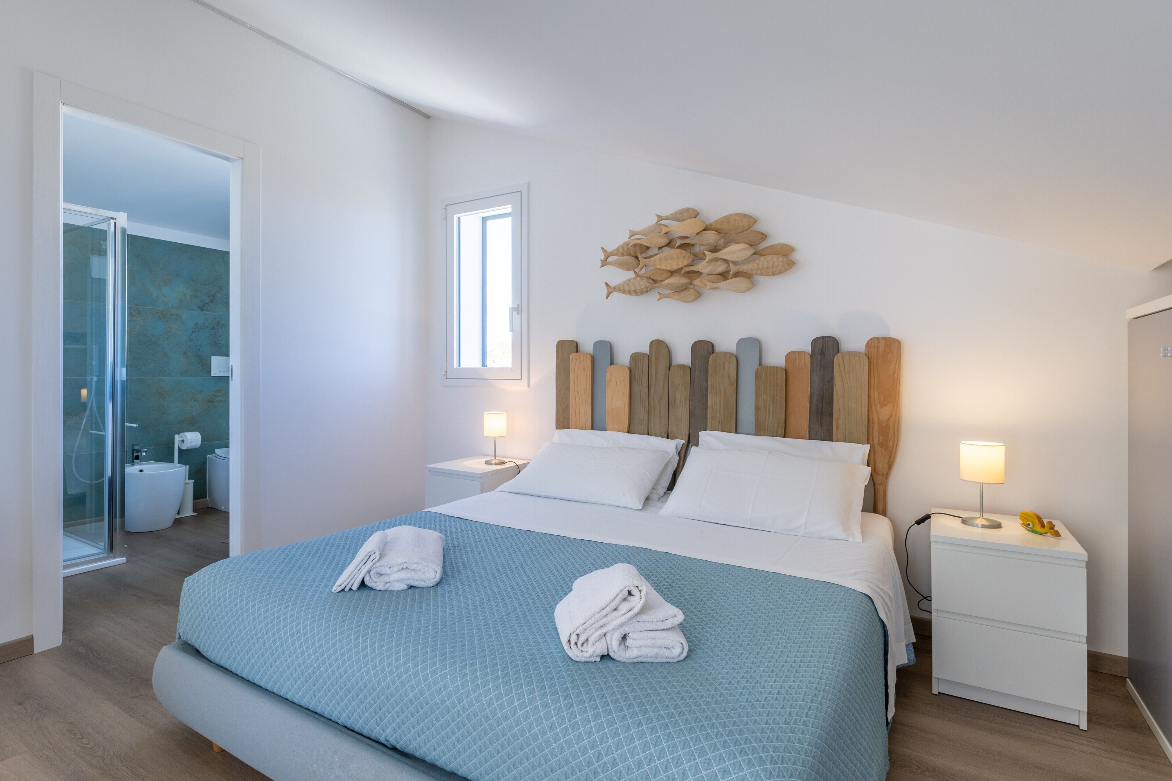 A hotel room with a bed, a nightstand, a wall-mounted fish decoration, and a bathroom visible through an open door.