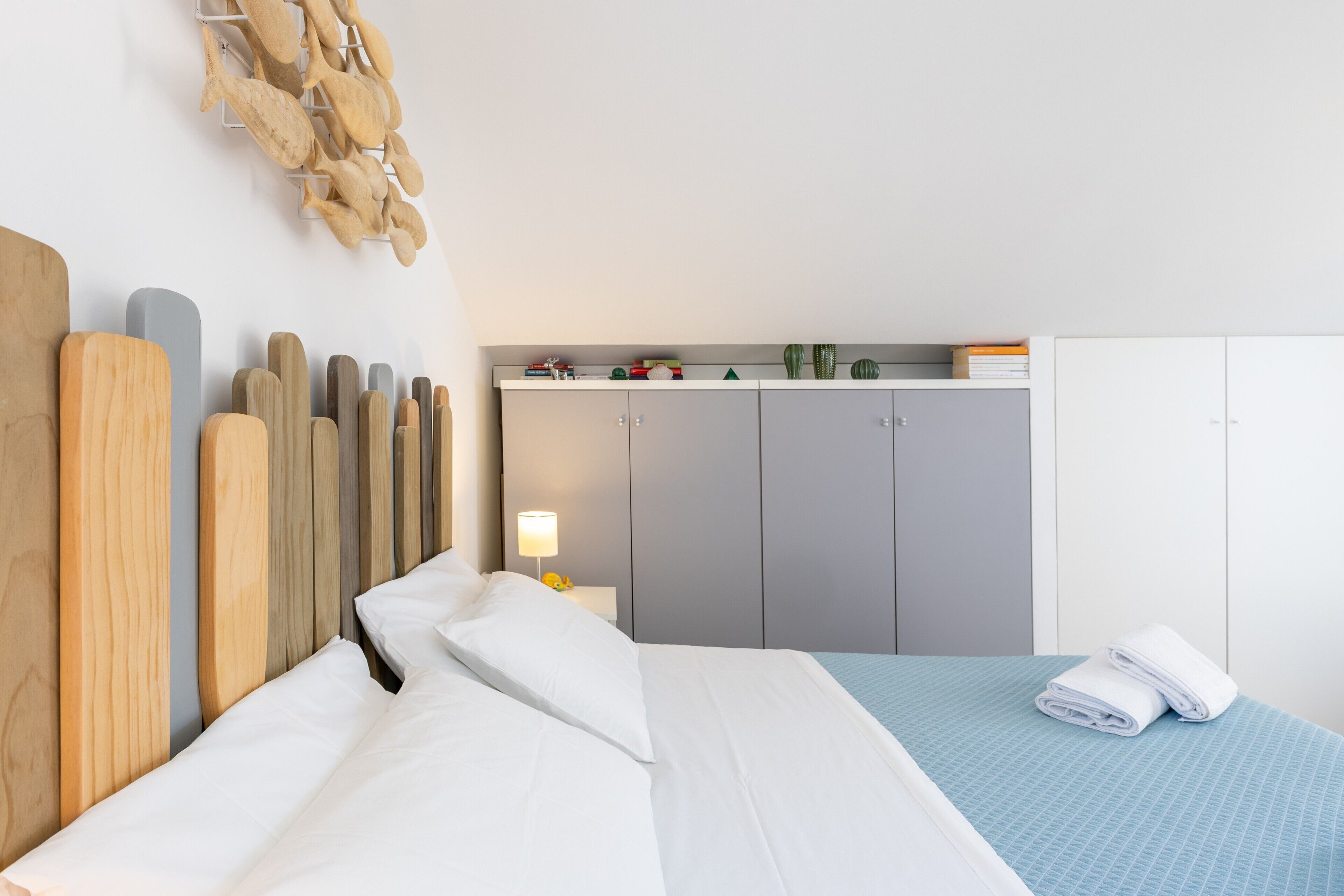 A neatly made bed with white linens, a wooden headboard, and a blue bedspread.