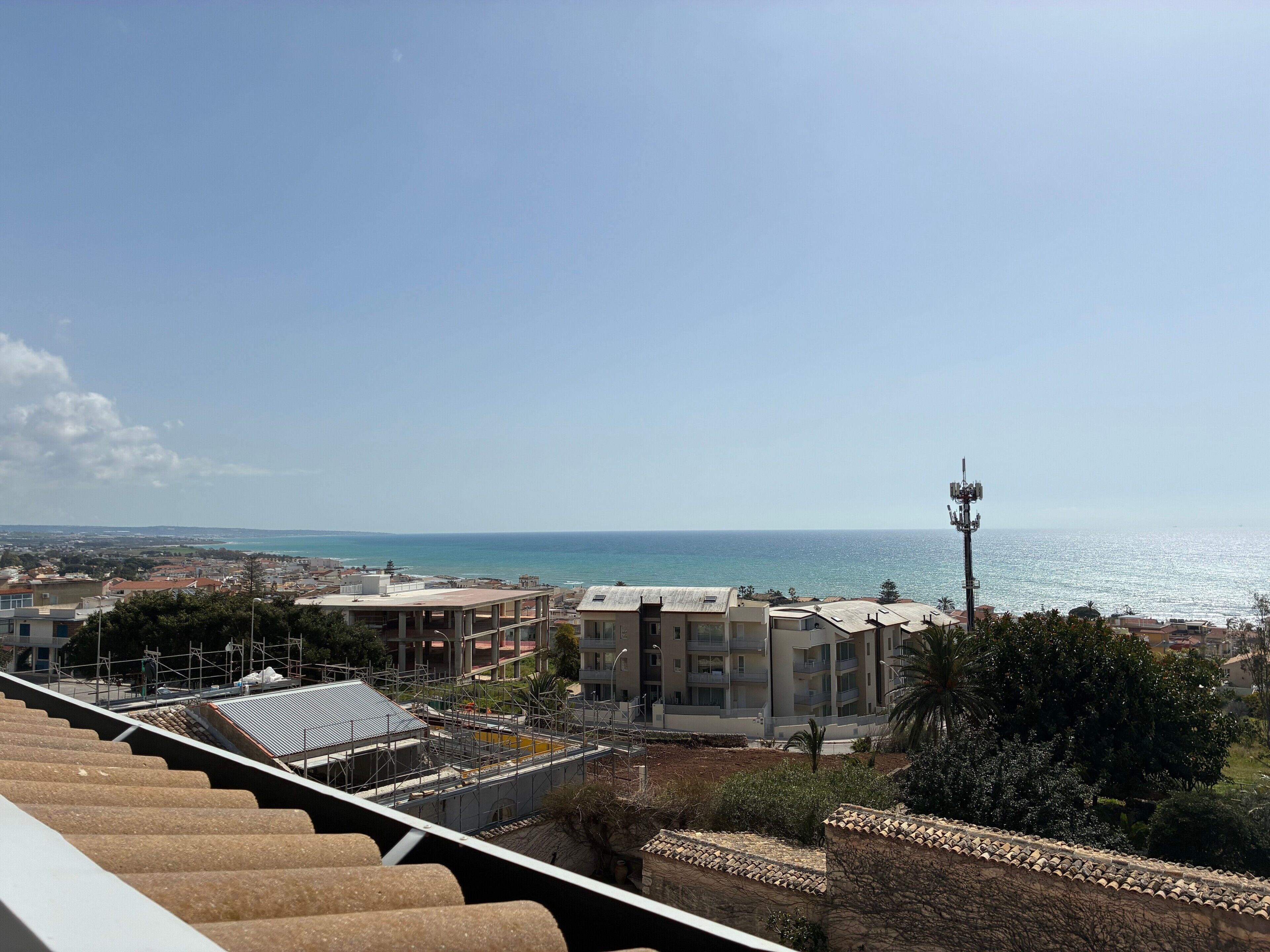 Paesaggio costiero con edifici, cielo sereno e mare in lontananza.