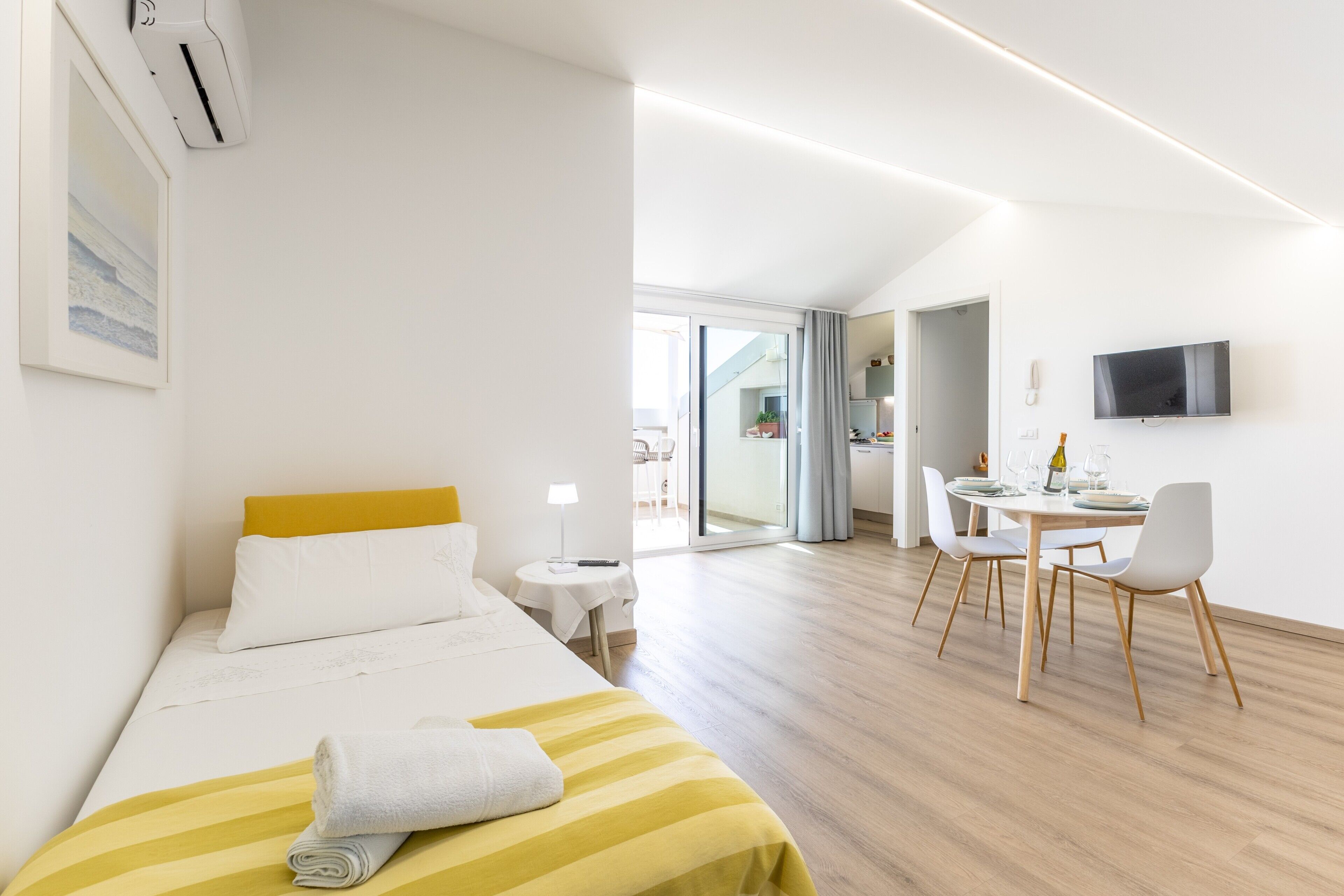 Une chambre d’hôtel moderne, équipée d’un lit, d’une petite table avec des chaises, d’un téléviseur fixé au mur et offrant une vue sur l’extérieur.