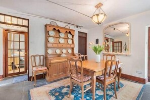 Ein Essbereich mit Holztisch und Stühlen, einem floralen Teppich, einer Wanduhr und einem Spiegel.