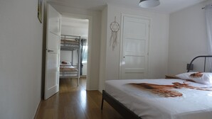 Um quarto com cama beliche, uma cama de solteiro, um sonho apanhado, uma porta e uma mesa de cabeceira.