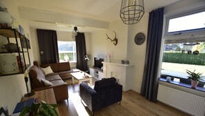 Uma sala de estar com sofá, mesa pequena, televisão, lareira e janela com vista para o exterior.