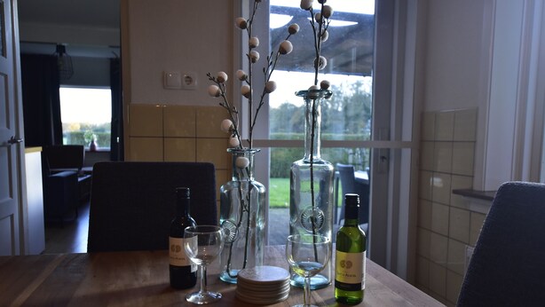 Uma mesa de jantar com copos de vinho, pratos e uma garrafa de vinho, em um quarto com janela e vista para o exterior.