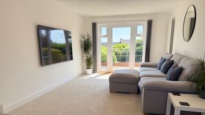 A modern living room with a grey sofa set, a white coffee table, and a large flat-screen TV mounted on the wall.