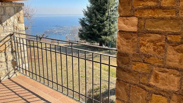 Un balcón con pared de piedra y barandilla metálica con vistas a la costa.