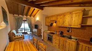 Una cocina con armarios de madera, una mesa de comedor de madera y un ventanal con cortinas.