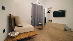 Ein modernes Schlafzimmer mit Bett, Nachttisch, einem kleinen Hocker, Fernseher und einem Vorhang.