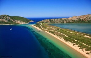 Vista aérea de un paisaje costero con mar azul cristalino, playa de arena y colinas verdes.