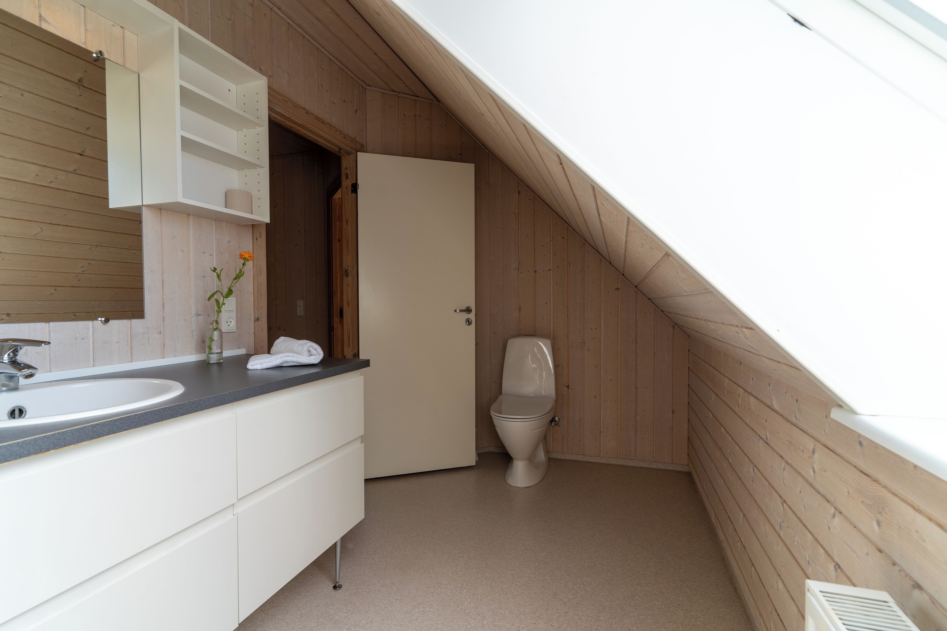 Een kleine badkamer met een schuin dak, een witte wastafel, spiegel en toilet.