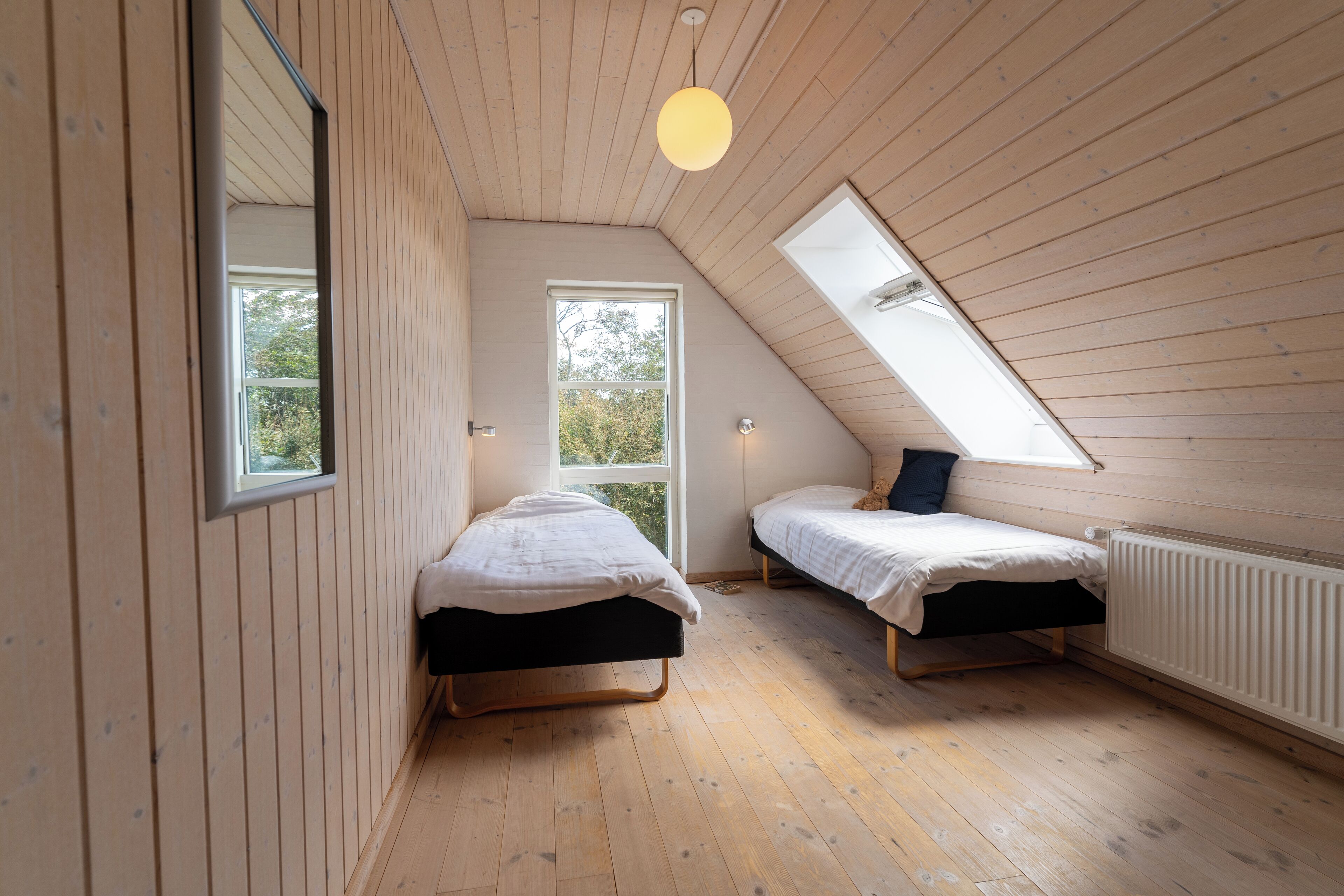 Un dormitorio estilo ático pequeño, con luz natural, dos camas, paredes de madera y un tragaluz.