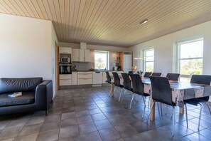 Une cuisine moderne avec des meubles blancs, un coin repas comprenant une table et des chaises, et un canapé en cuir noir.