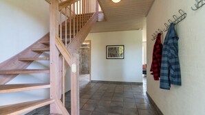 A wooden staircase leading to a second floor, a tiled floor, and a wall with a coat rack holding two jackets. - Feriehuset Østersvej (Fjerritslev)