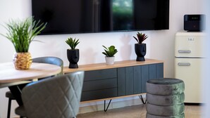 Ein modernes Zimmer mit einem Holztisch, Stühlen, einem Fernseher, einem Schrank und Topfpflanzen.