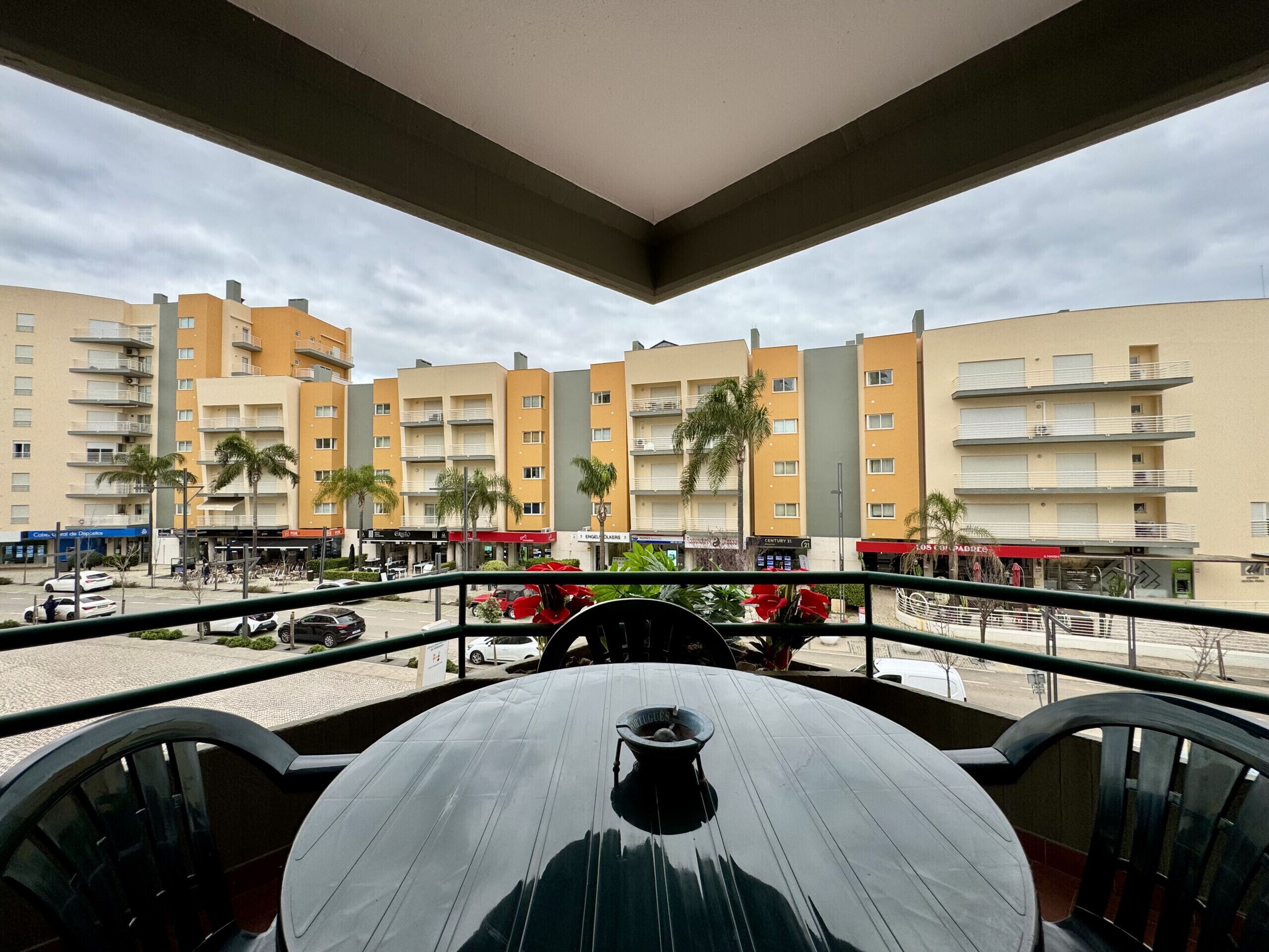 A balcony with a table and chairs, overlooking a street with buildings and palm trees.