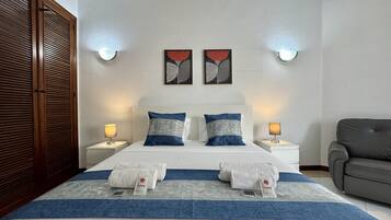 A hotel room with a double bed, two nightstands, a grey armchair, and artwork on the walls.
