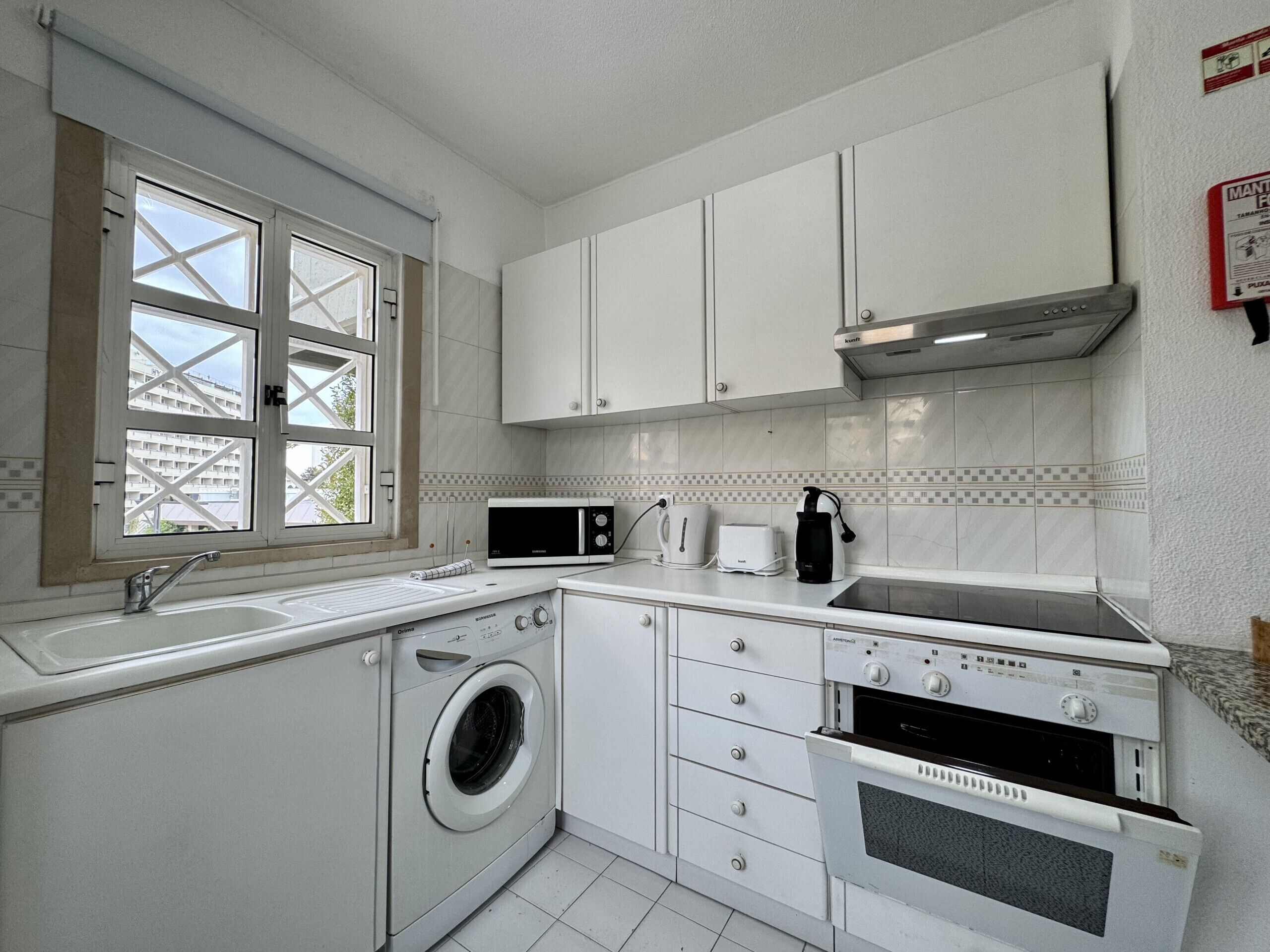 A compact kitchen with white cabinets, a washing machine, a microwave, a toaster, and a coffee maker.