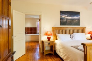 Un dormitorio con cama de madera, dos mesitas de noche con lámparas, un cuadro en la pared y vistas a un viñedo.