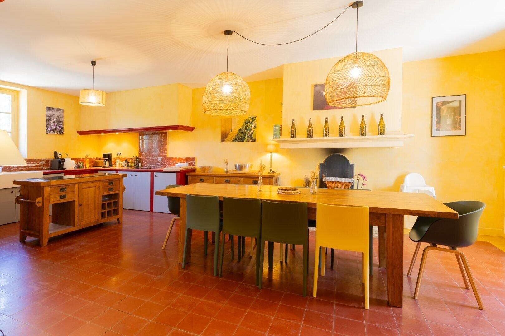 Cozinha com ilha de madeira, mesa de jantar, cadeiras, luminárias pendentes e adega na parede.