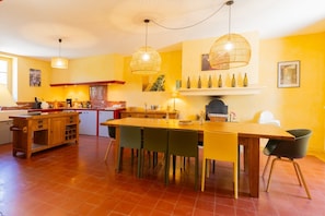 Una cocina con una isla de madera, mesa de comedor, sillas, lámparas colgantes y una estantería para vinos en la pared.
