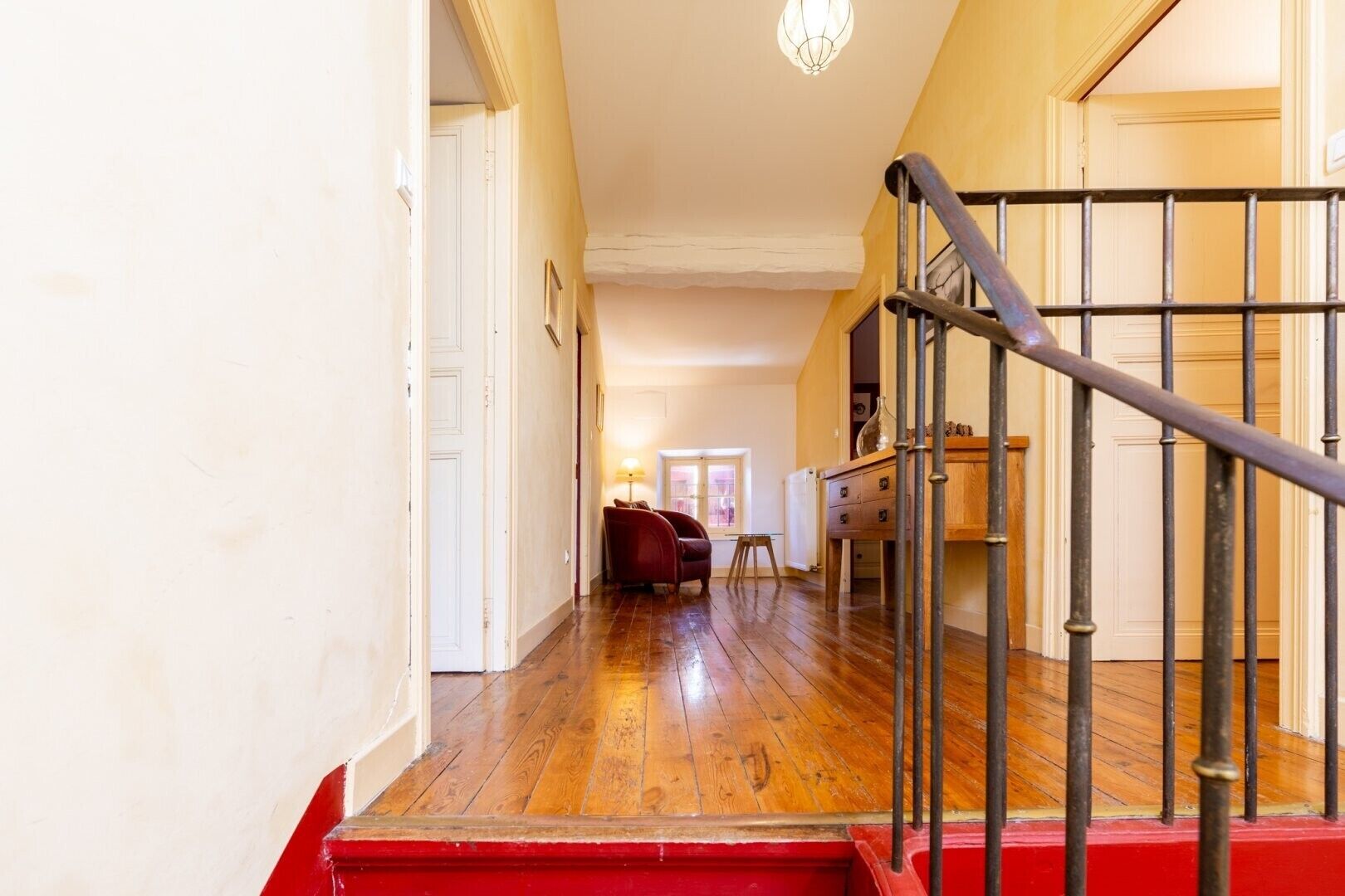 Una escalera con barandilla de metal que lleva a un rellano, pisos de madera y un zócalo rojo.