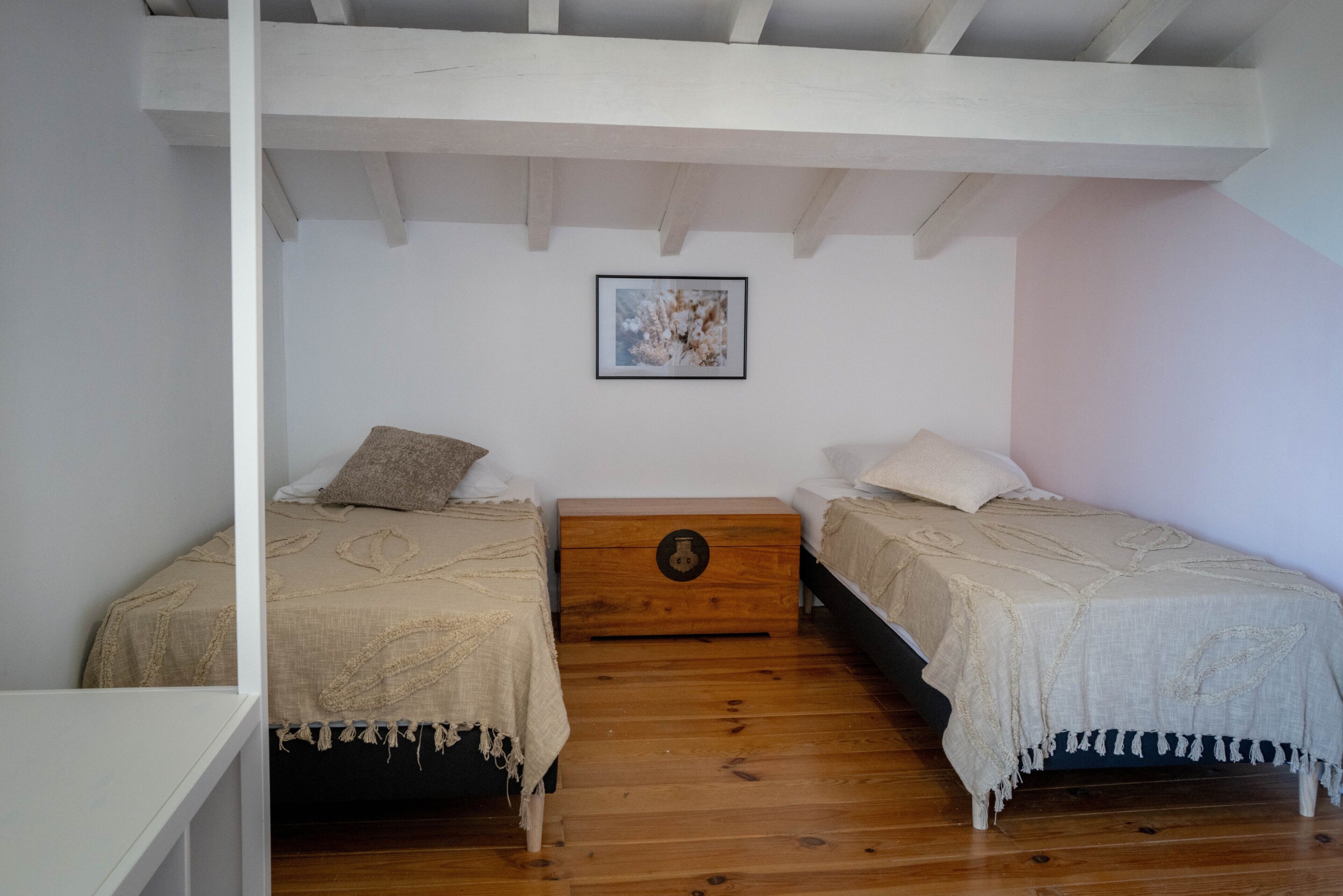 Ein Schlafzimmer mit zwei Betten, Holzboden, weißer Decke und einem gerahmten Bild an der Wand.