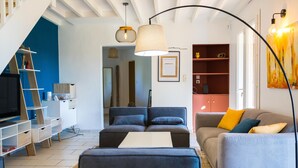 A modern living room with a sofa, ottoman, and a television. There is a ladder, a bookshelf, and a painting on the wall. - Bastide des Vignes: Private Pool and Tranquility on a Vineyard Estate (Trèbes)