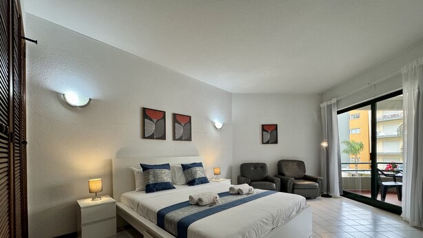 Une chambre d’hôtel moderne avec un grand lit, deux tables de chevet, une chaise et une vue sur le balcon extérieur.