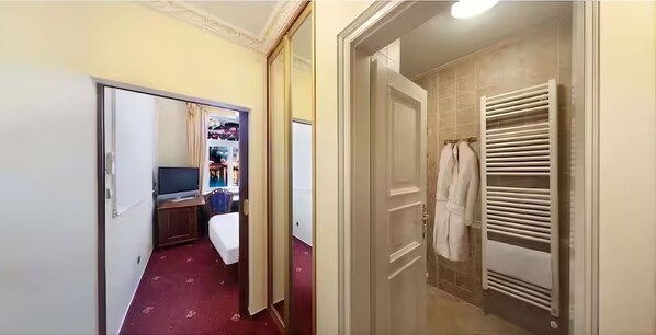 A hotel room with a bed, a TV, a wardrobe, and a bathroom with a towel rack. - Hotel General (Prague)